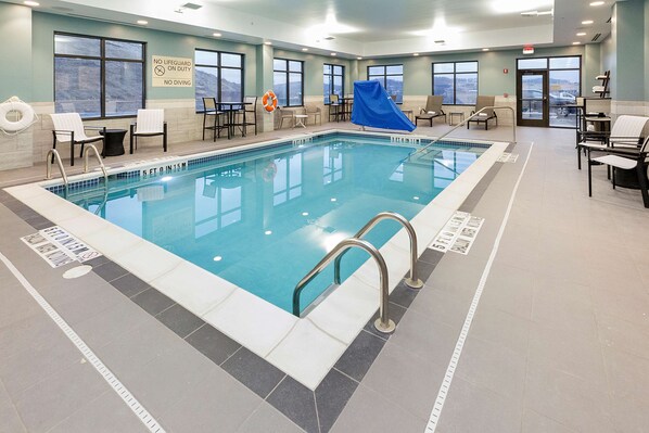 Piscina interior con señalización de seguridad visible, una silla para salvavidas y vistas al exterior a través de grandes ventanales.