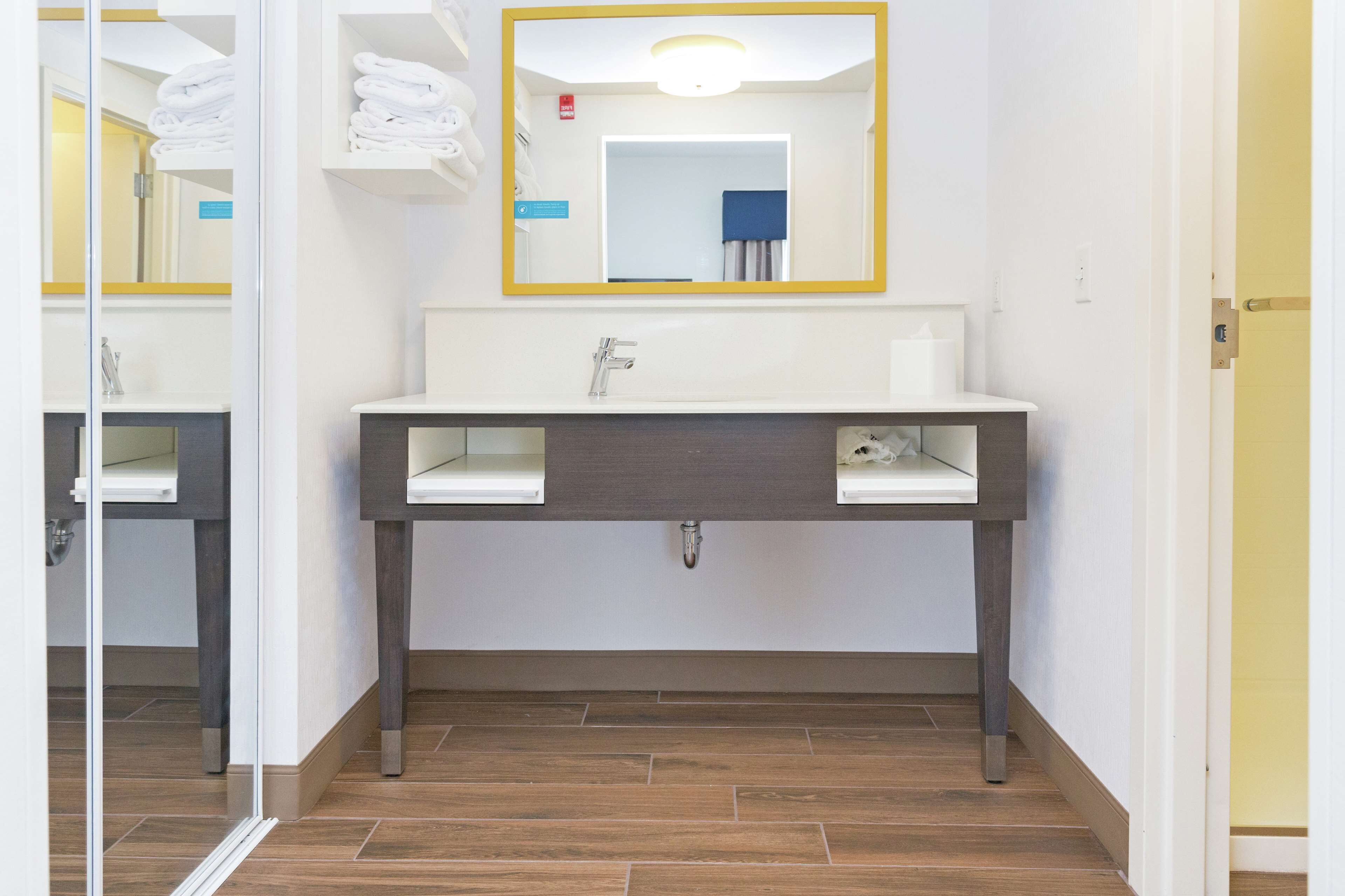 A bathroom with a white sink, dark wooden vanity, and a mirror with a yellow frame.