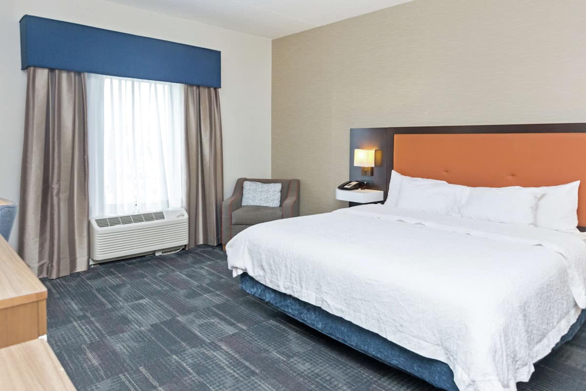 A hotel room with a large bed, a chair, a desk, and a window with curtains.