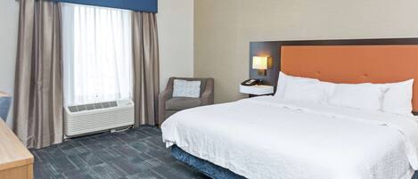 A hotel room with a large bed, a chair, a desk, and a window with curtains.