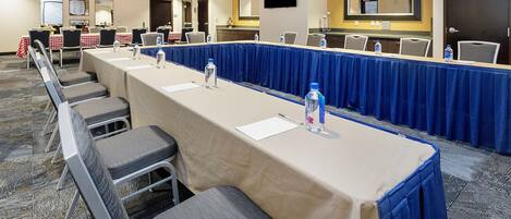 A conference room with a long table, chairs, water bottles, and a TV on the wall.