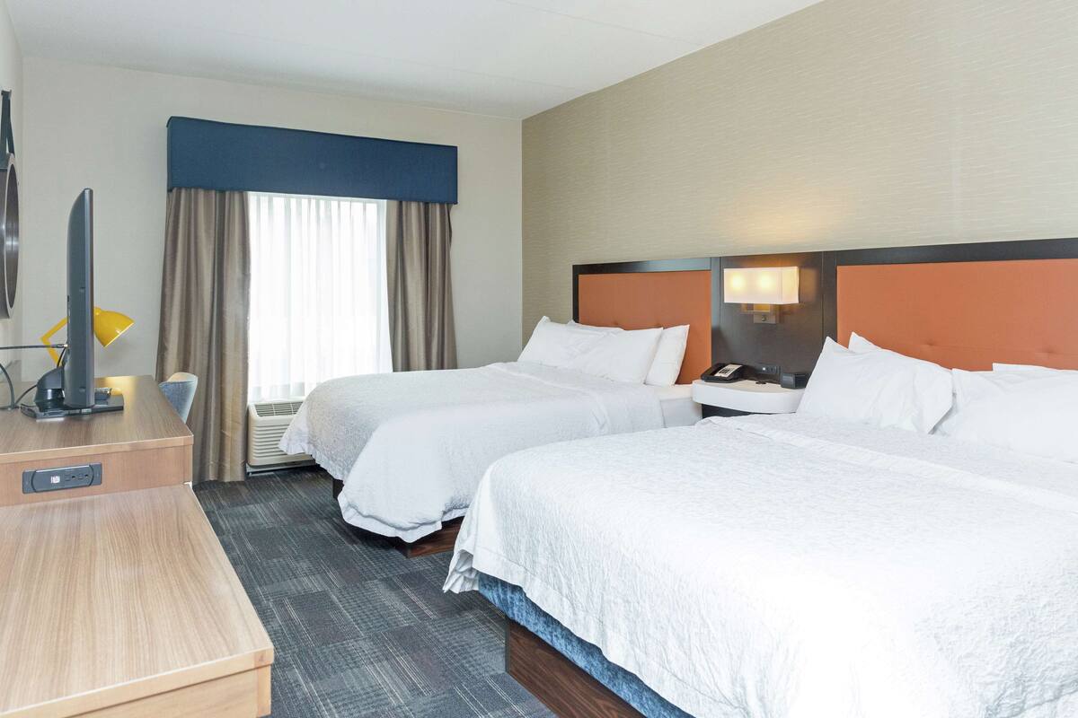 A hotel room with two beds, a desk with a lamp, and a television.