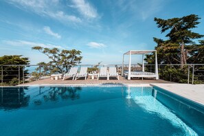 Un espace aménagé au bord de la piscine, avec des chaises longues et un coin salon abrité, offrant une vue panoramique.
