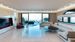 A modern living room with a flat-screen TV, a red chair, a sofa, and a coffee table. - Villa Azure (Vari-Voula-Vouliagmeni)