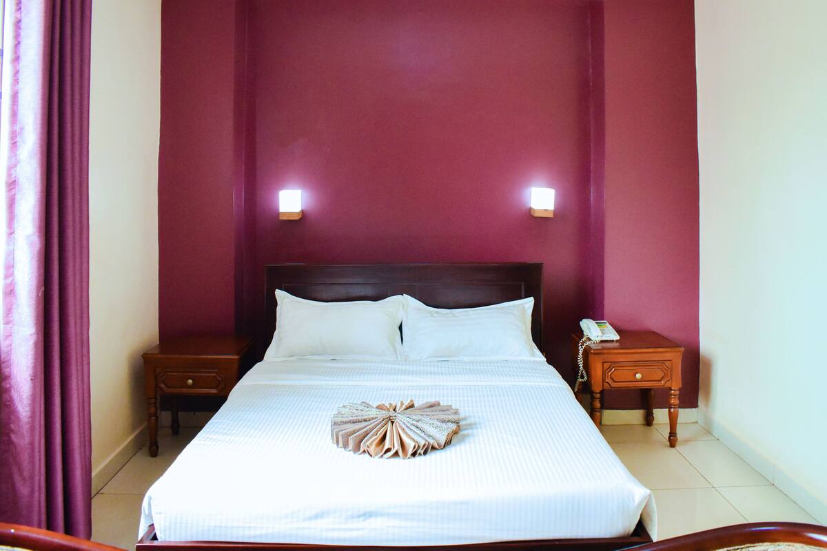 A neatly made bed with a towel centerpiece, two bedside tables, and a phone on one of the tables.