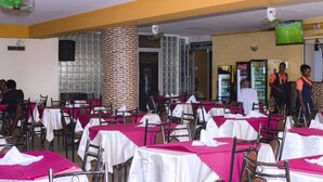 Een restaurant met tafels bedekt met witte en roze tafelkleden, stoelen en een aan de muur bevestigde televisie.