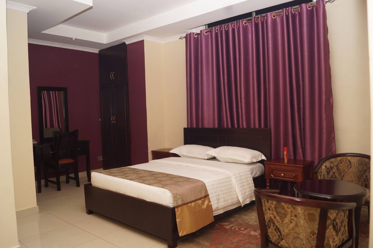A hotel room with a bed, a desk, a chair, and a small table.