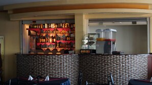 Een bar met flessen op planken, een koffieapparaat en tafels met servetten.