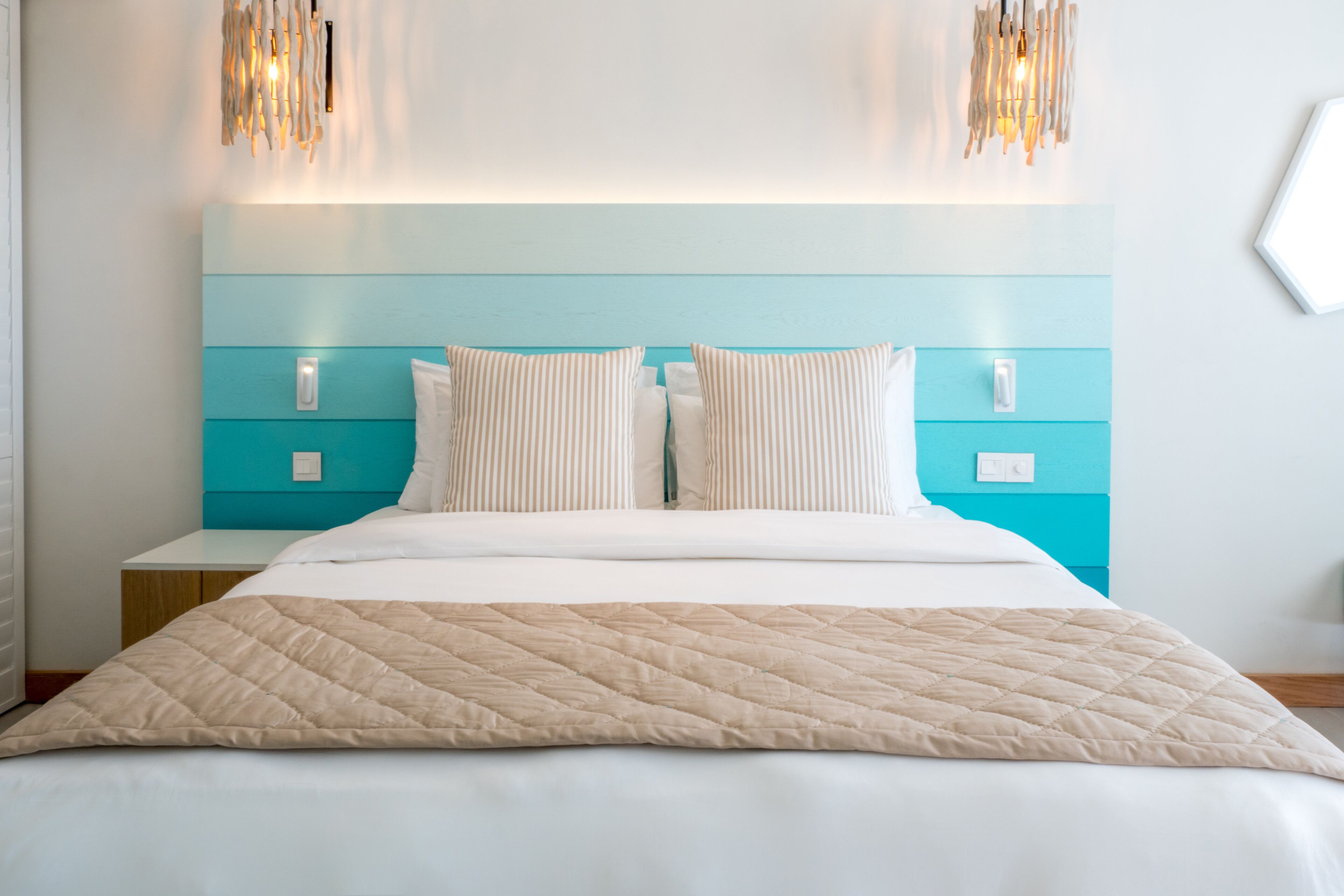 A neatly made bed with a quilted blanket, a turquoise headboard, and two bedside tables with light switches.