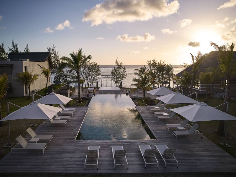 A poolside area with lounge chairs and umbrellas, overlooking a body of water and a sunset.