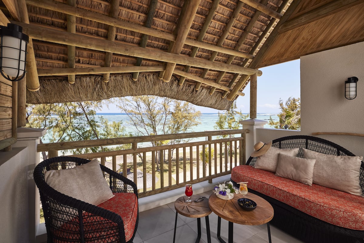 A covered outdoor seating area with wicker furniture, a wooden table, and a view of the ocean.