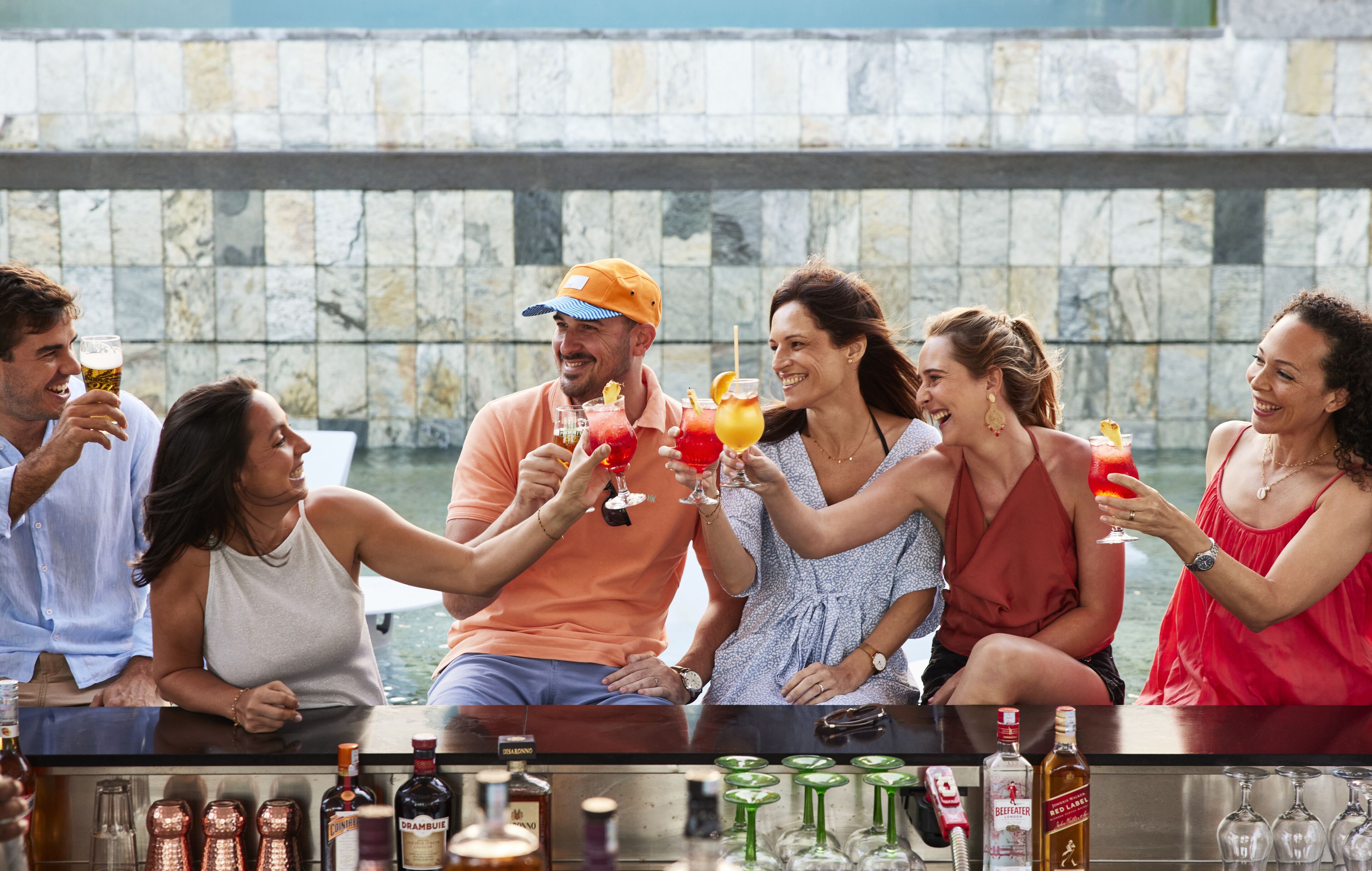 A group of people toasting with drinks at a bar with a stone wall backdrop.