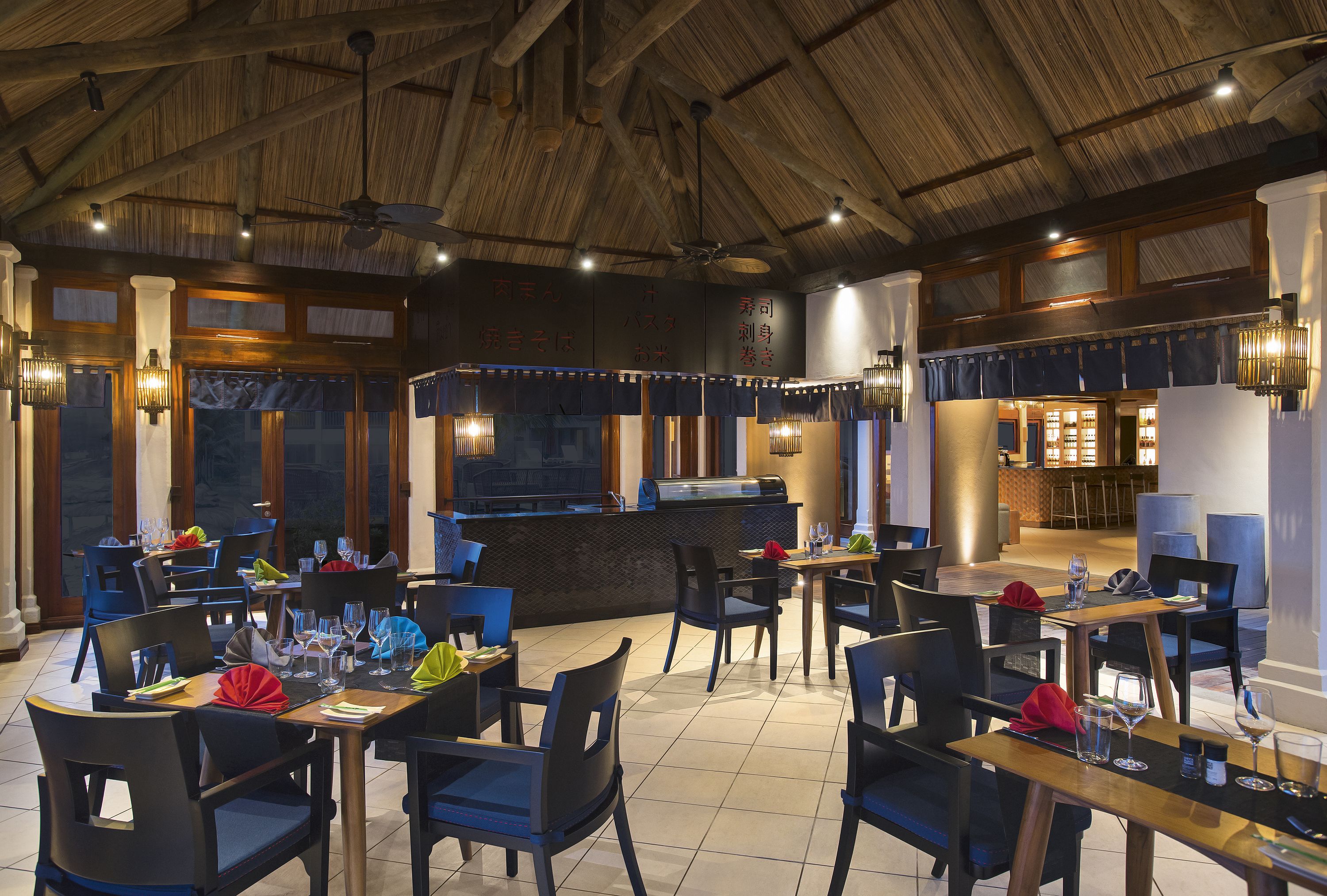 A restaurant with wooden ceiling beams, black chairs, and tables set with wine glasses and napkins.