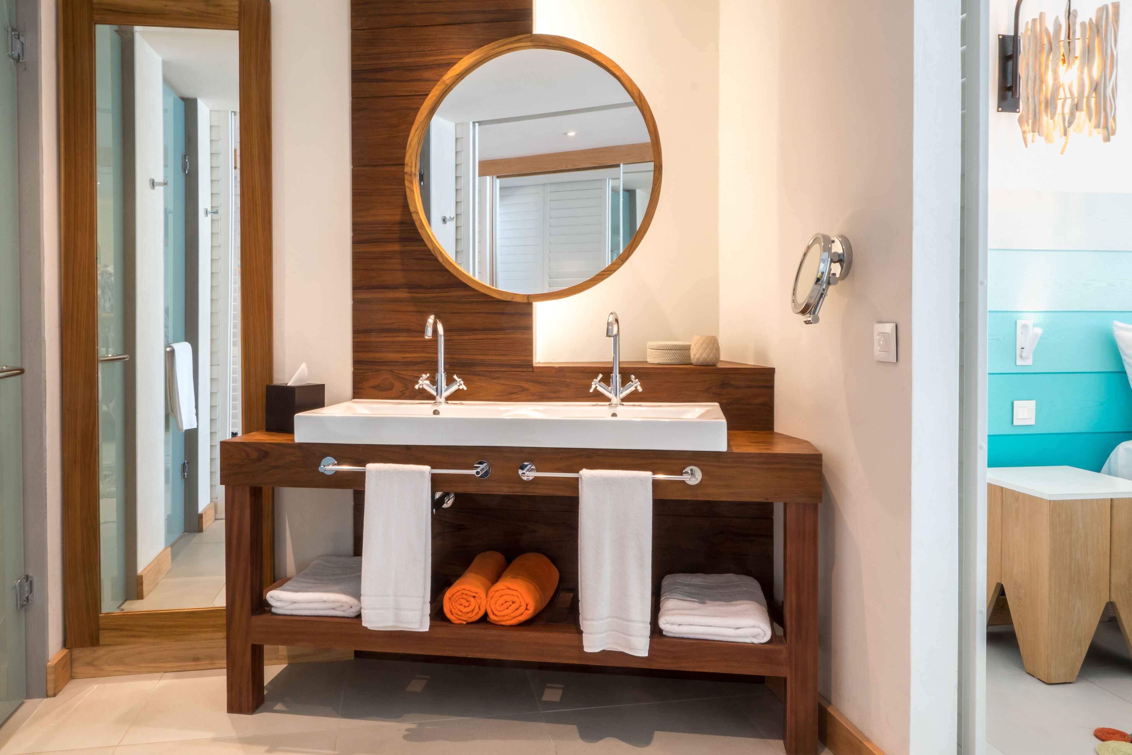 Un baño moderno con tocador de madera, un espejo redondo e lavamanos doble.