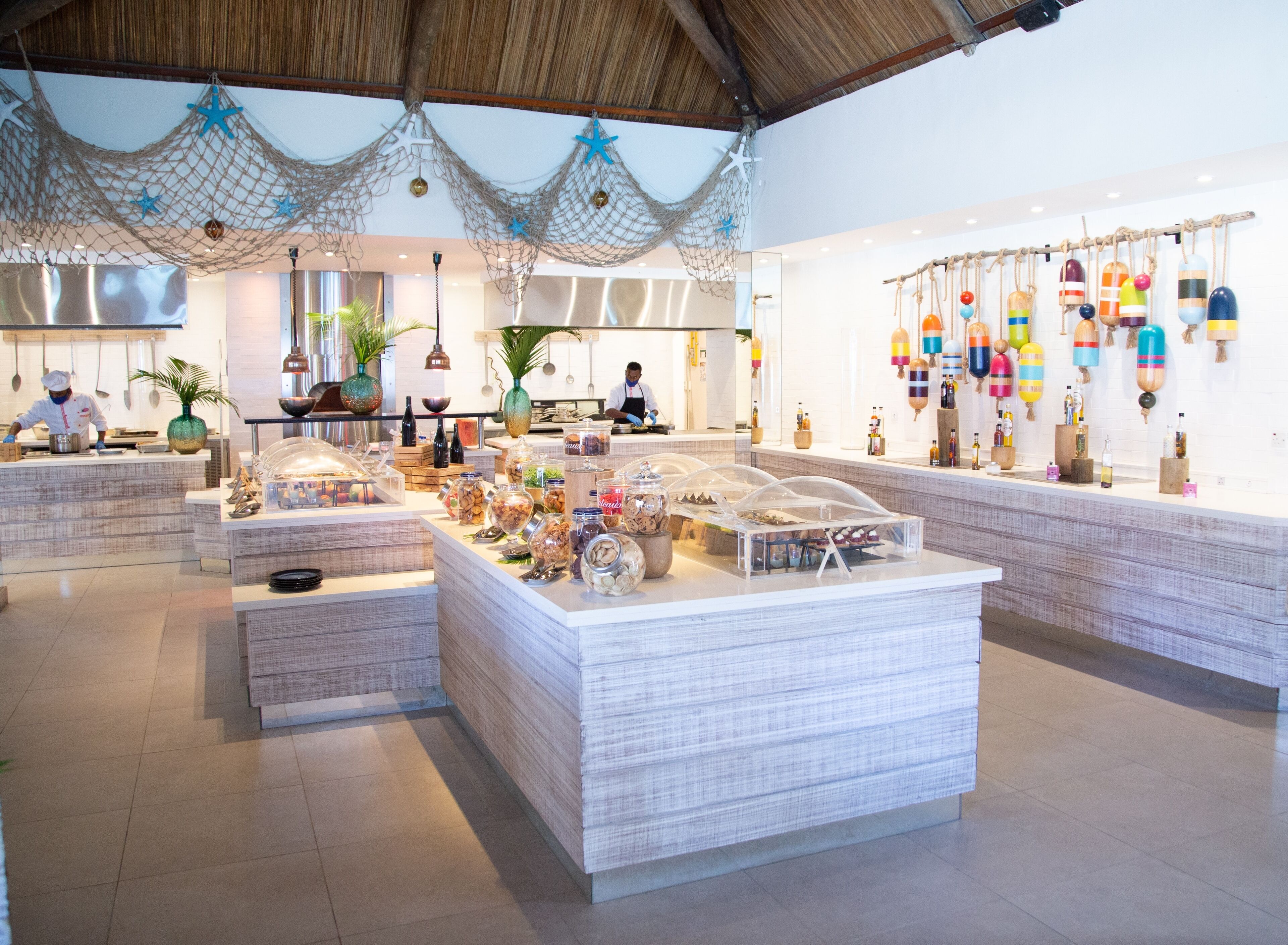 A modern hotel lobby with a central reception desk, decorative netting, and a wall display of colorful bottles.