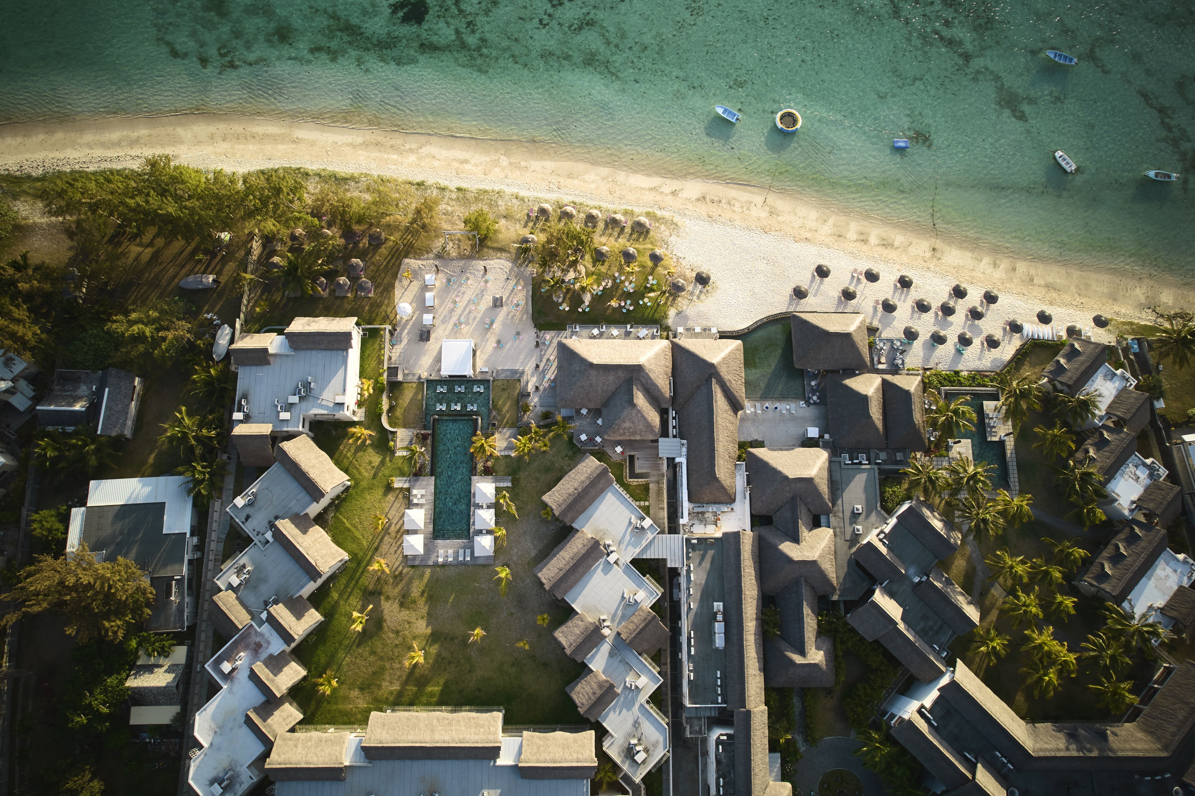 Vista aérea de un resort con varias cabañas, una piscina central y una playa con barcos.