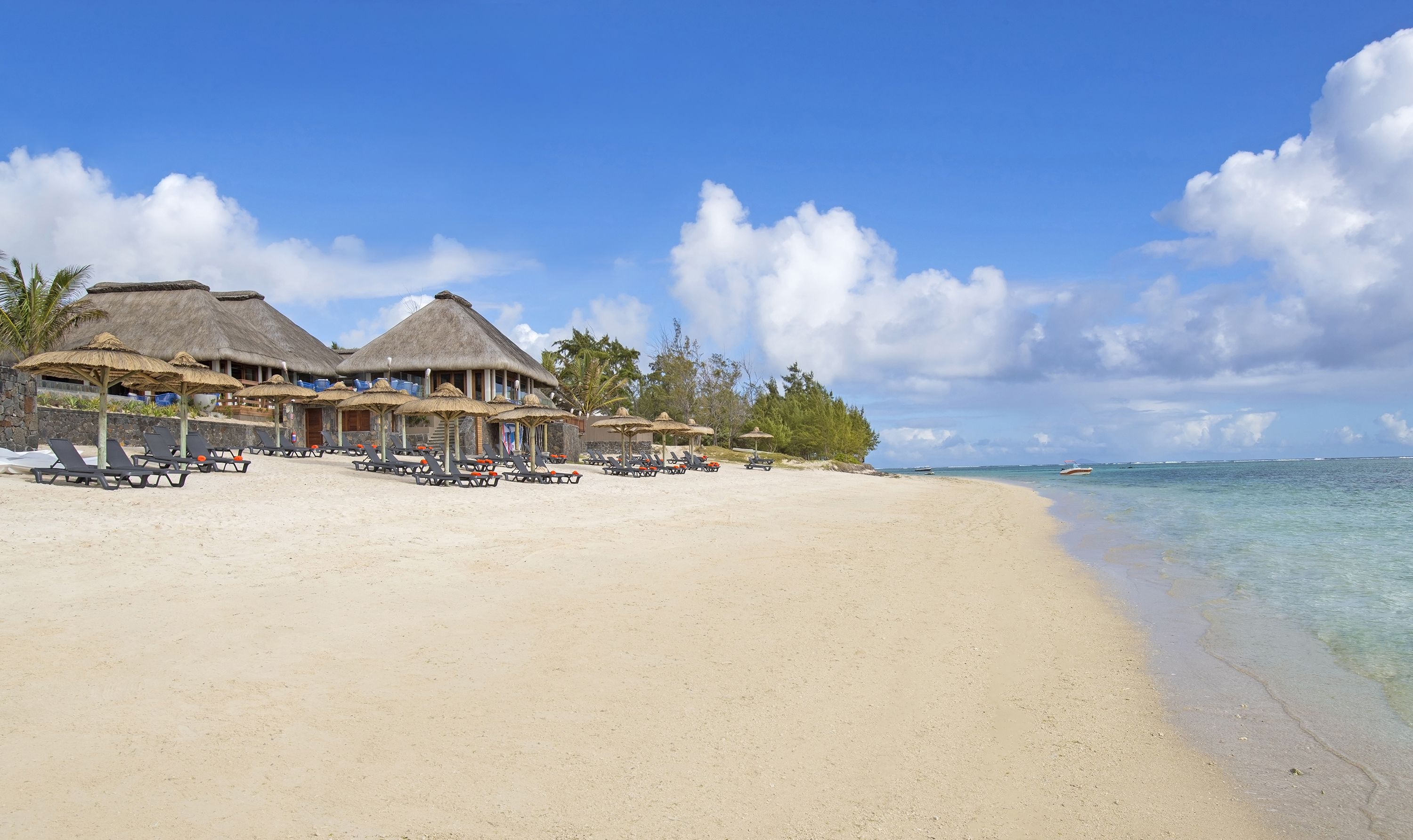 A beach resort with thatched-roof buildings, sun loungers, and clear turquoise waters.