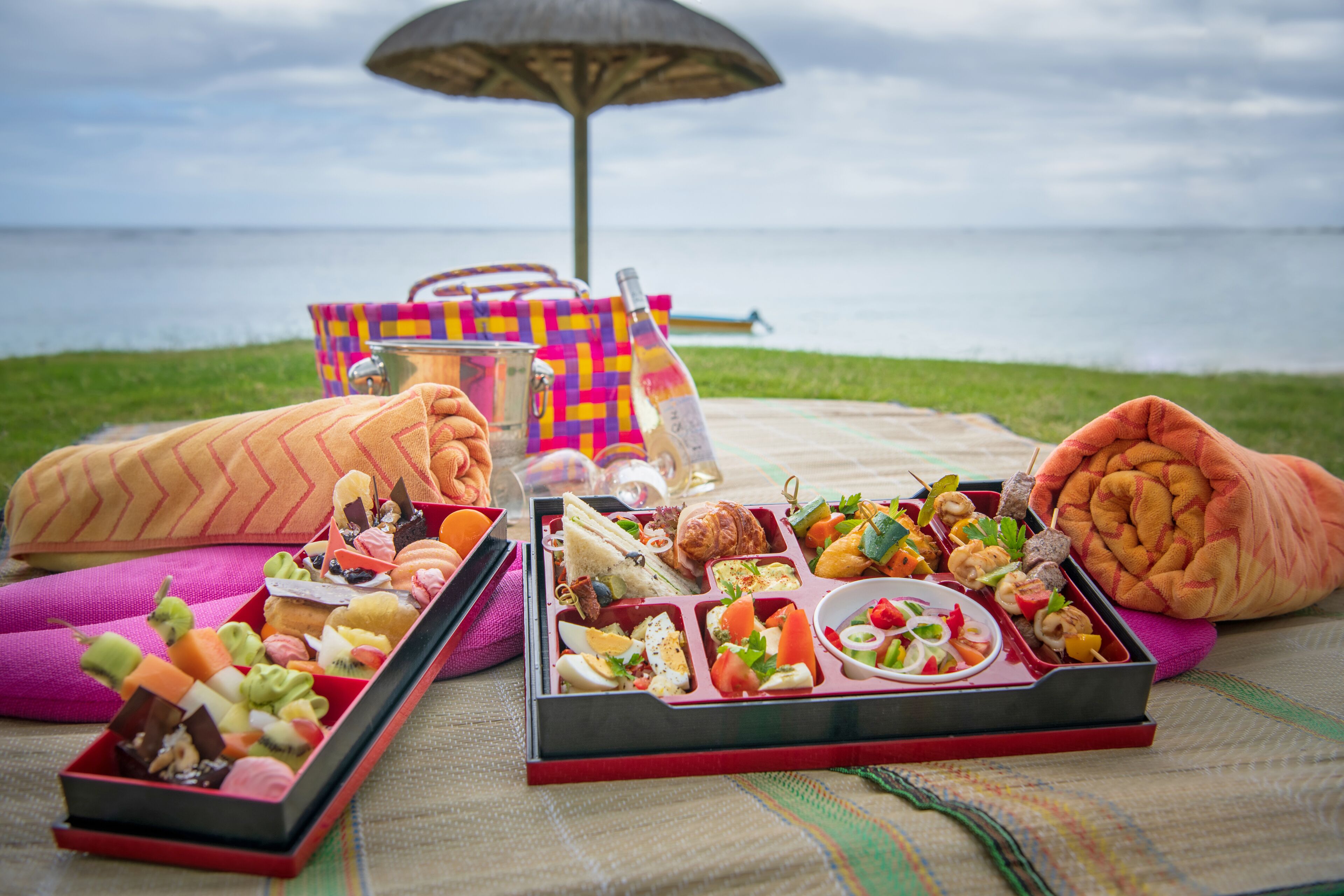 A picnic setup with a variety of food items on a blanket by the water.