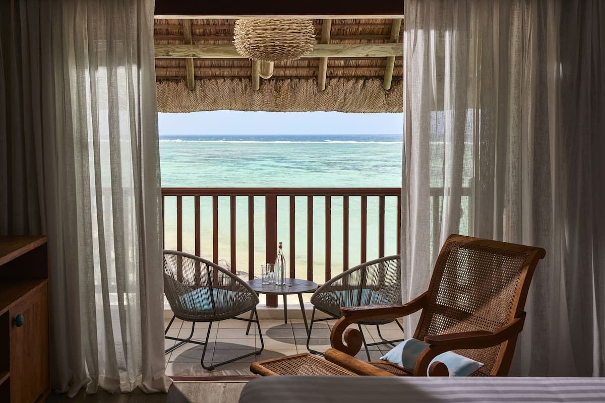 A balcony with a view of the ocean, wicker chairs, a small table with glasses, and a wooden chair.