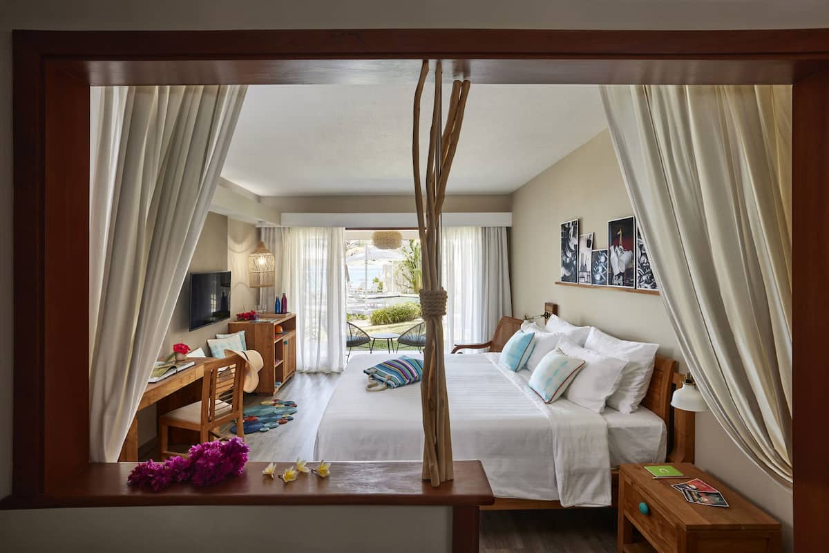 A hotel room with a bed, a desk, a chair, a TV, and a view of the outside.