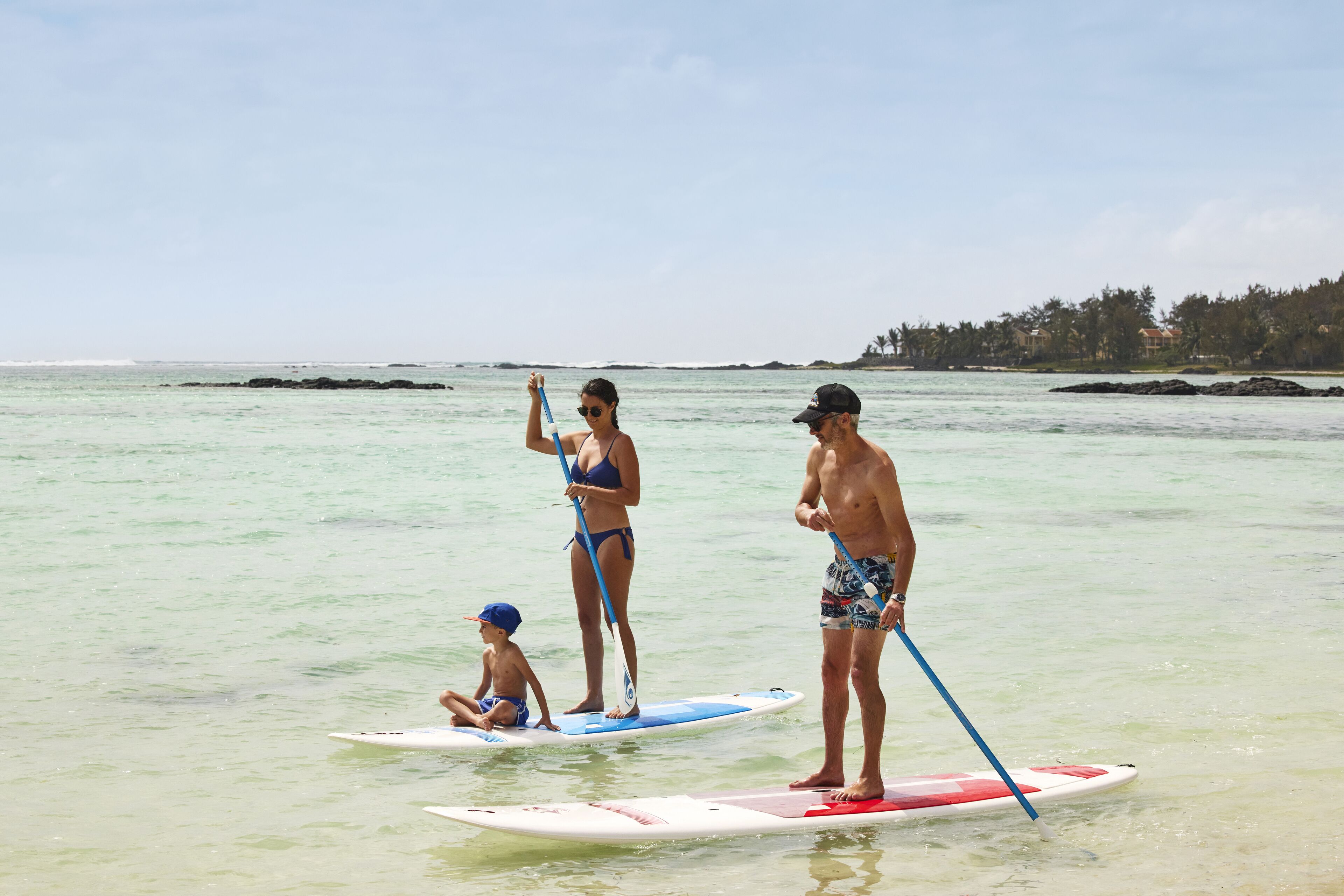 Tres personas haciendo paddleboard en un mar tranquilo con cielos despejados.