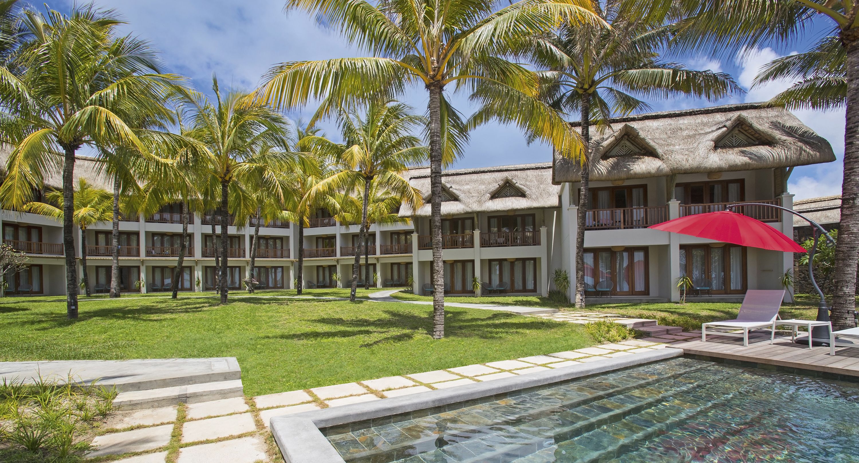 A resort with a pool, palm trees, and a building with a thatched roof.