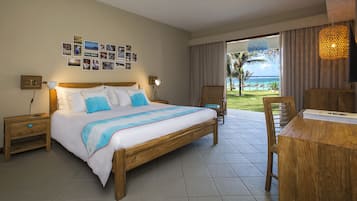 A hotel room with a bed, a desk, a chair, a nightstand, a wall with photos, and a view of the ocean.