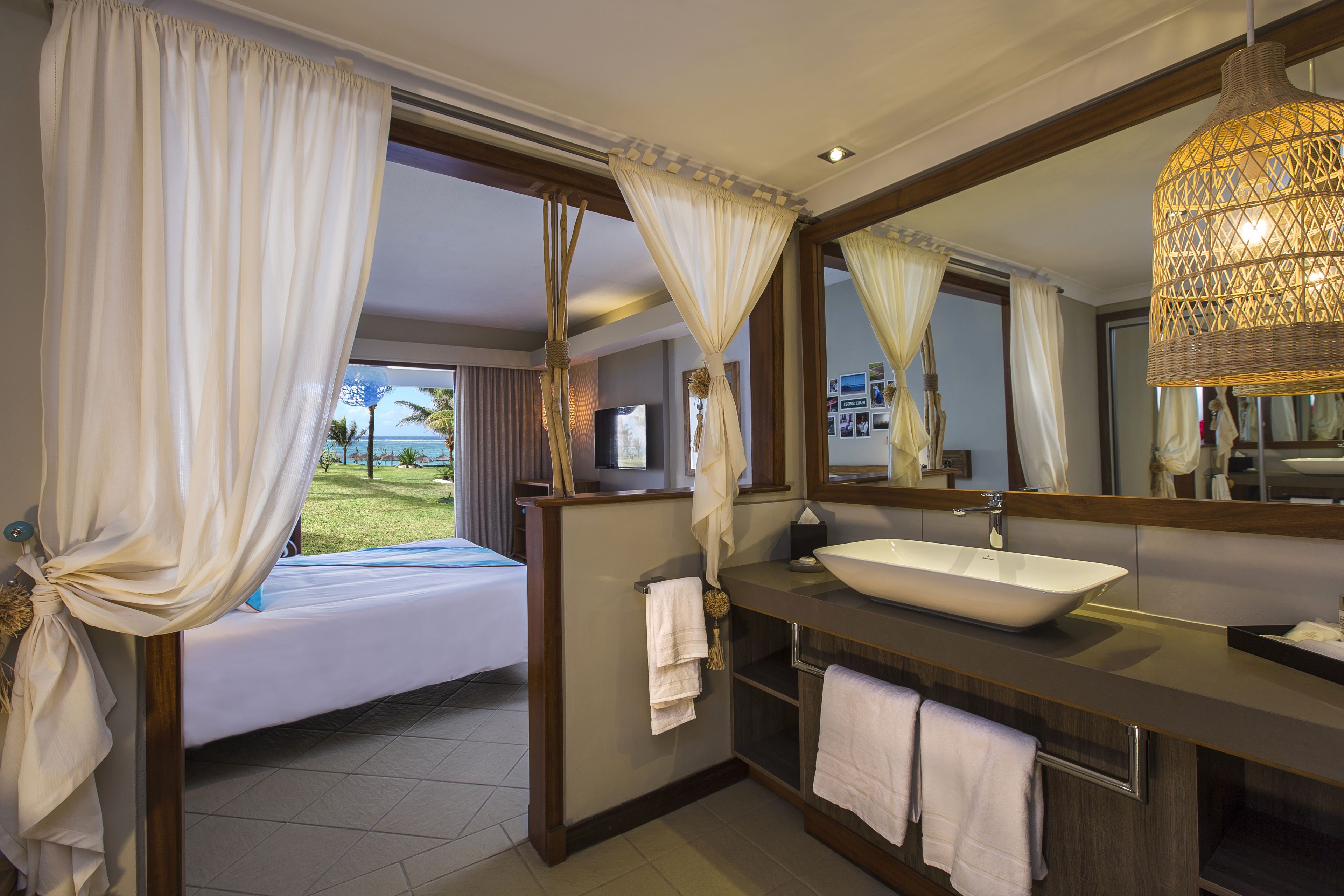 A hotel room with a bed, a large mirror, a bathroom with a sink, and curtains.