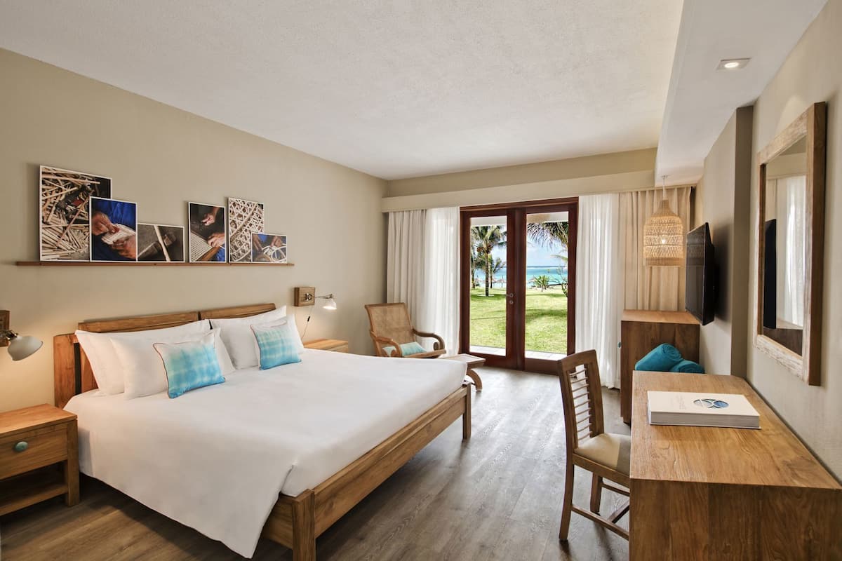 A hotel room with a bed, a desk, a chair, a TV, and a view of the outdoors.