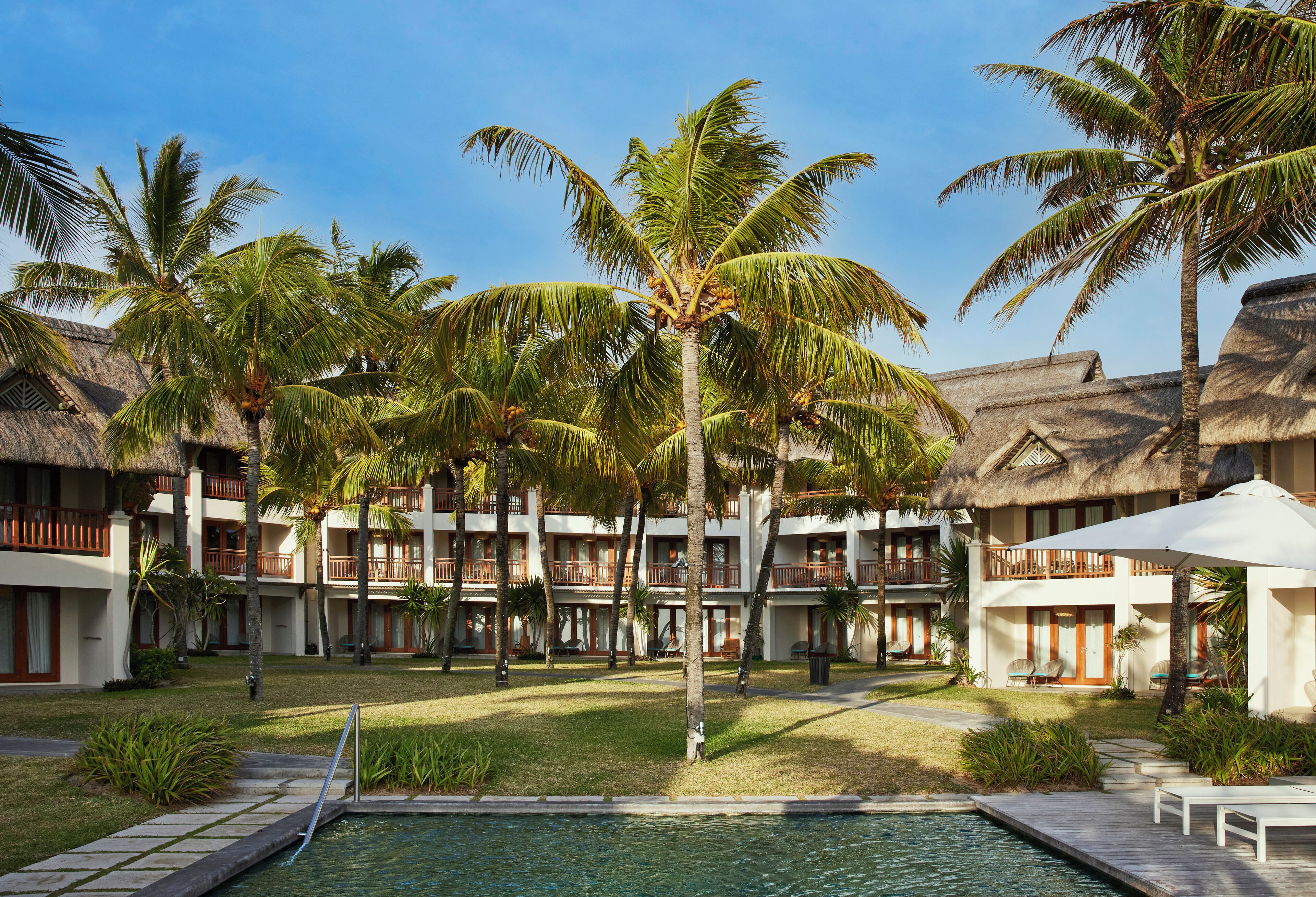 A resort with multiple-story buildings, a swimming pool, and palm trees.