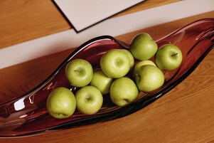 Un tazón de vidrio con varias manzanas verdes sobre una superficie de madera.