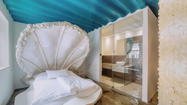 Un dormitorio moderno con una cama curva distintiva, una pared de vidrio y un techo azul.