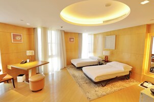 A hotel room with a desk, two beds, a chair, and a small table.