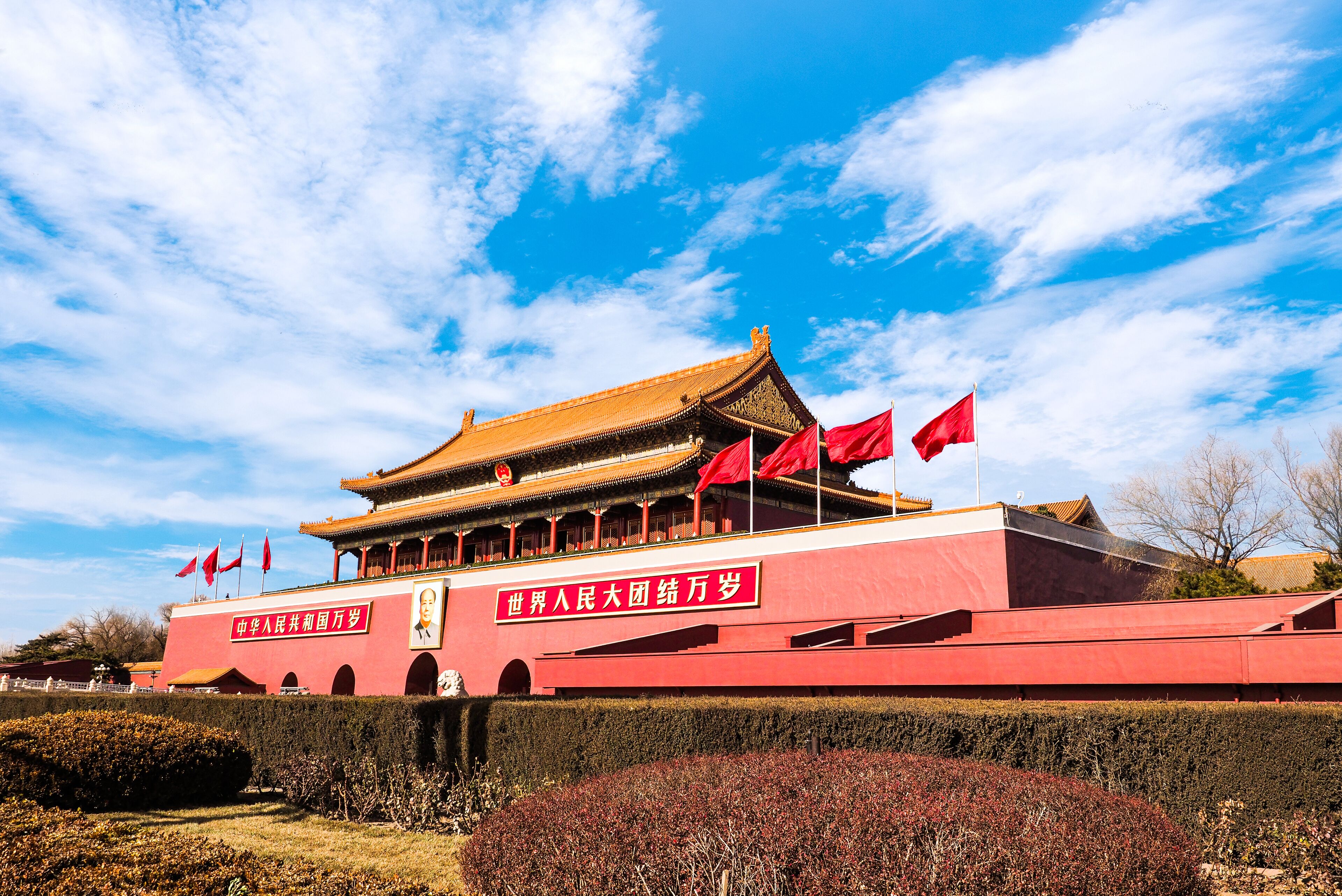 Un grand bâtiment rouge, doté d’un toit traditionnel et orné de plusieurs drapeaux rouges.