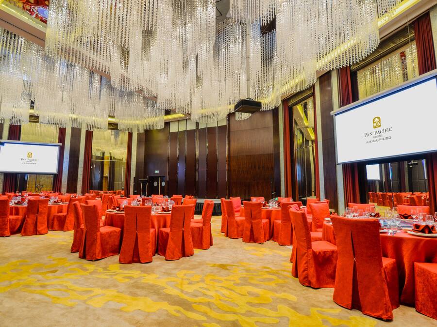 A banquet hall with tables set for a formal event, featuring a large screen displaying the hotel's name.