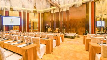 A conference room with rows of tables and chairs, a podium, and a large screen.