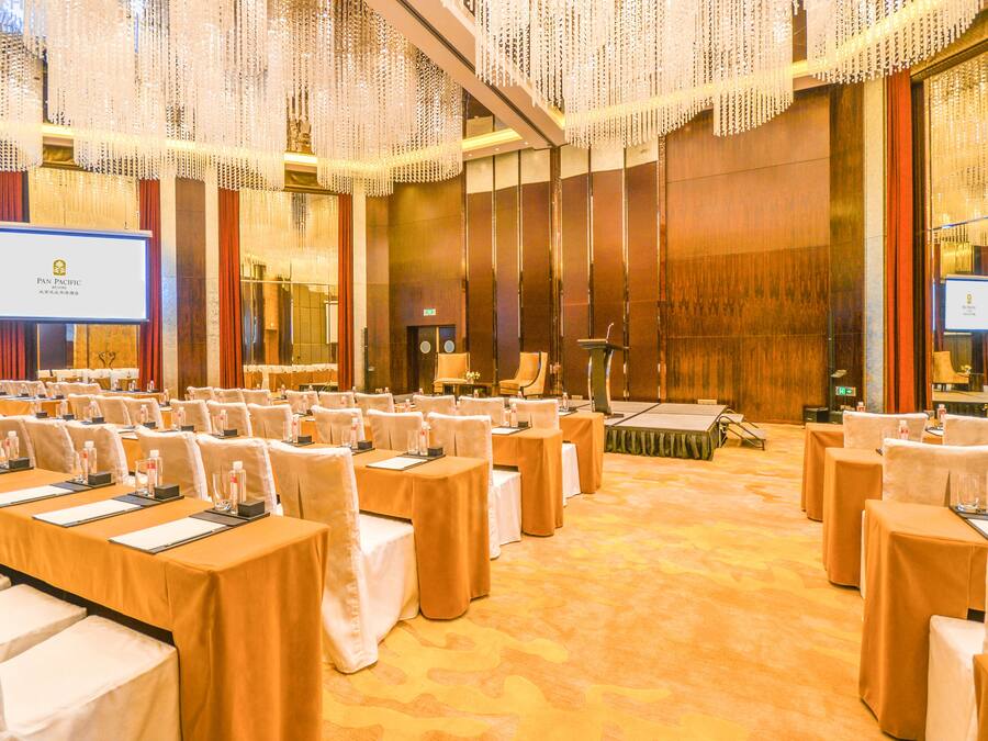 A conference room with rows of tables and chairs, a podium, and a large screen.