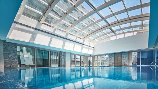 Una piscina interior con techo de vidrio, ventanas amplias y suelo de baldosas.