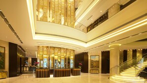 Un moderno vestíbulo de hotel con un mostrador de recepción central, una escalera y techos altos.