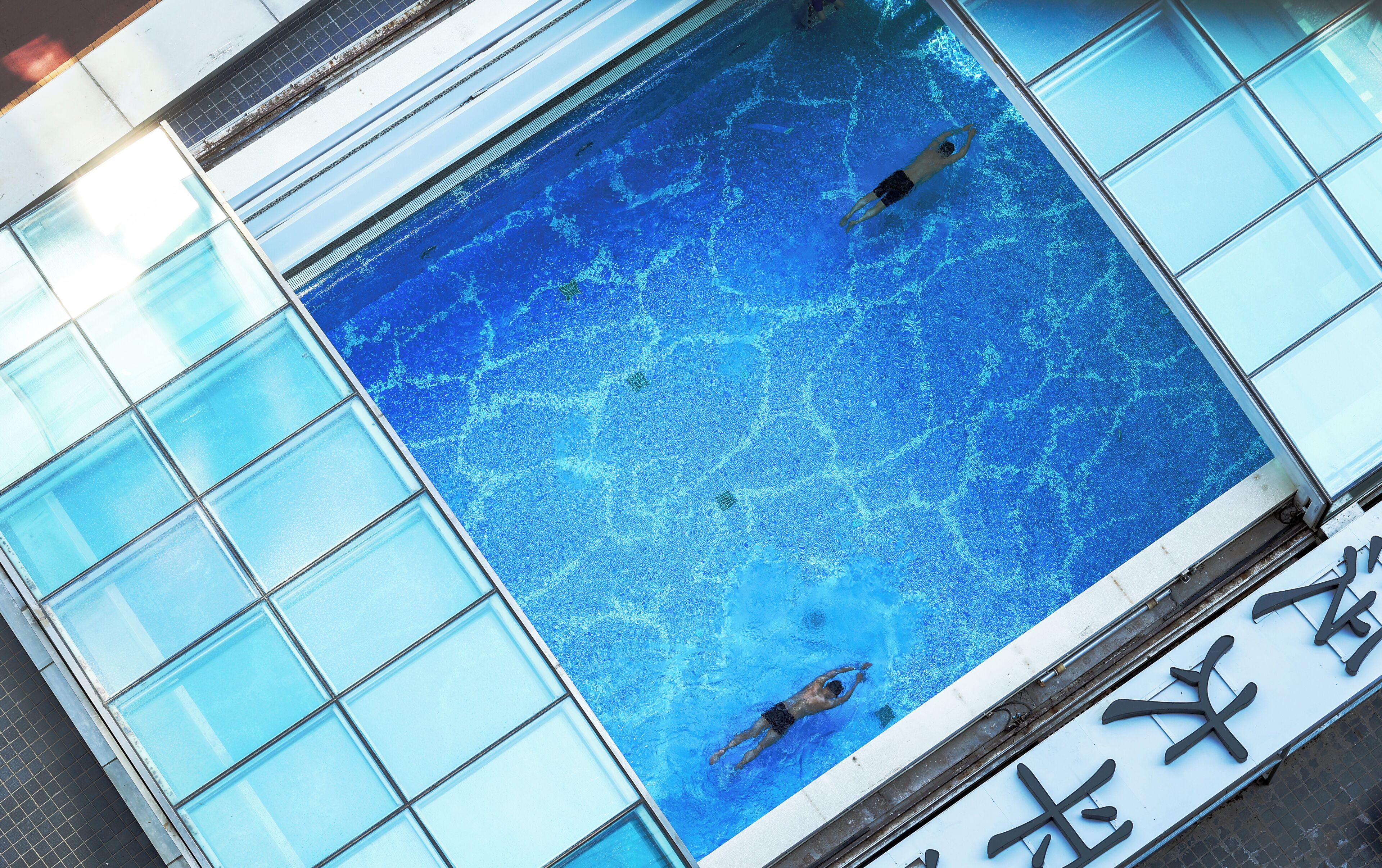 Una piscina con agua azul cristalina, rodeada de paneles de vidrio.