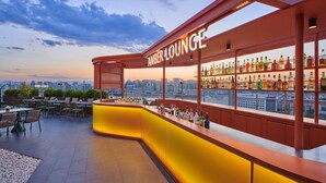 Un bar en la azotea con vistas a la ciudad, que cuenta con una barra y una zona de estar.