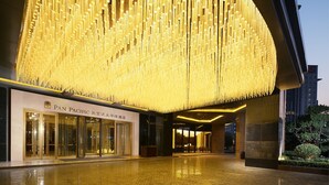 Entrada de hotel con un gran candelabro iluminado, fachada moderna y un vestíbulo bien iluminado.