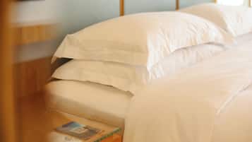 A neatly made bed with white linens and a wooden nightstand with a magazine.