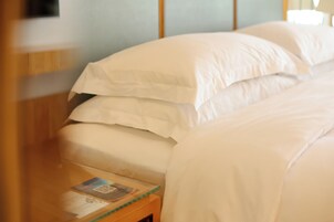 A neatly made bed with white linens and a wooden nightstand with a magazine.