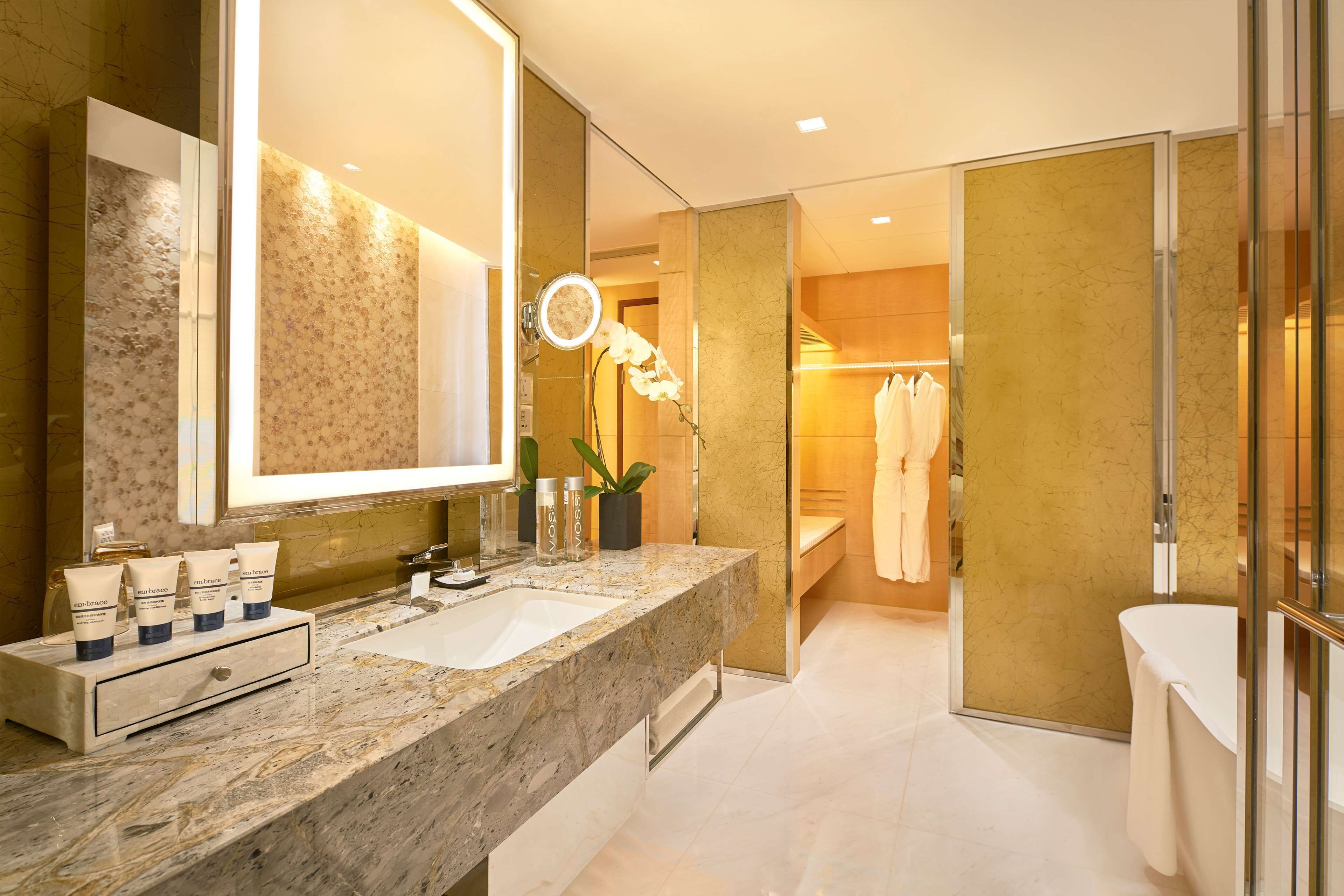 A modern bathroom with a marble countertop, a large mirror, and a vanity with toiletries.