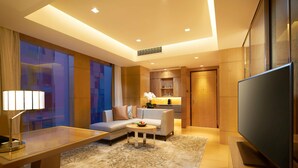 Habitación de hotel moderna con sofá, una mesa de centro, televisión y escritorio con lámpara.