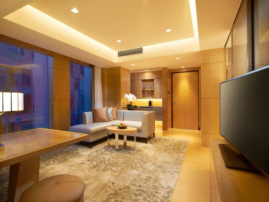 Habitación de hotel moderna con sofá, una mesa de centro, televisión y escritorio con lámpara.