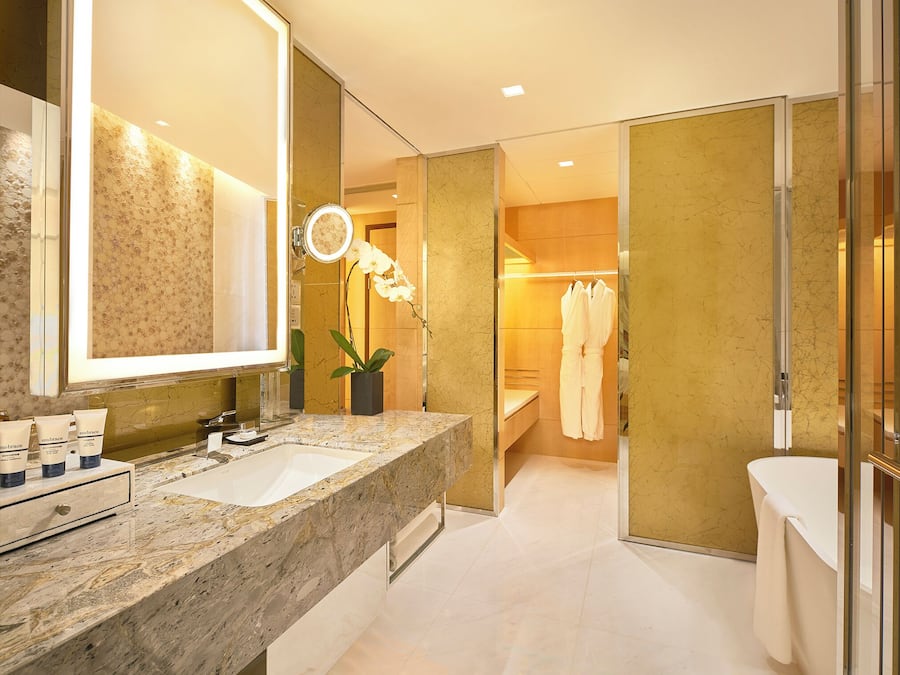 Un baño moderno con lavamanos de mármol, un espejo grande, un perchero para bata y una orquídea en maceta.