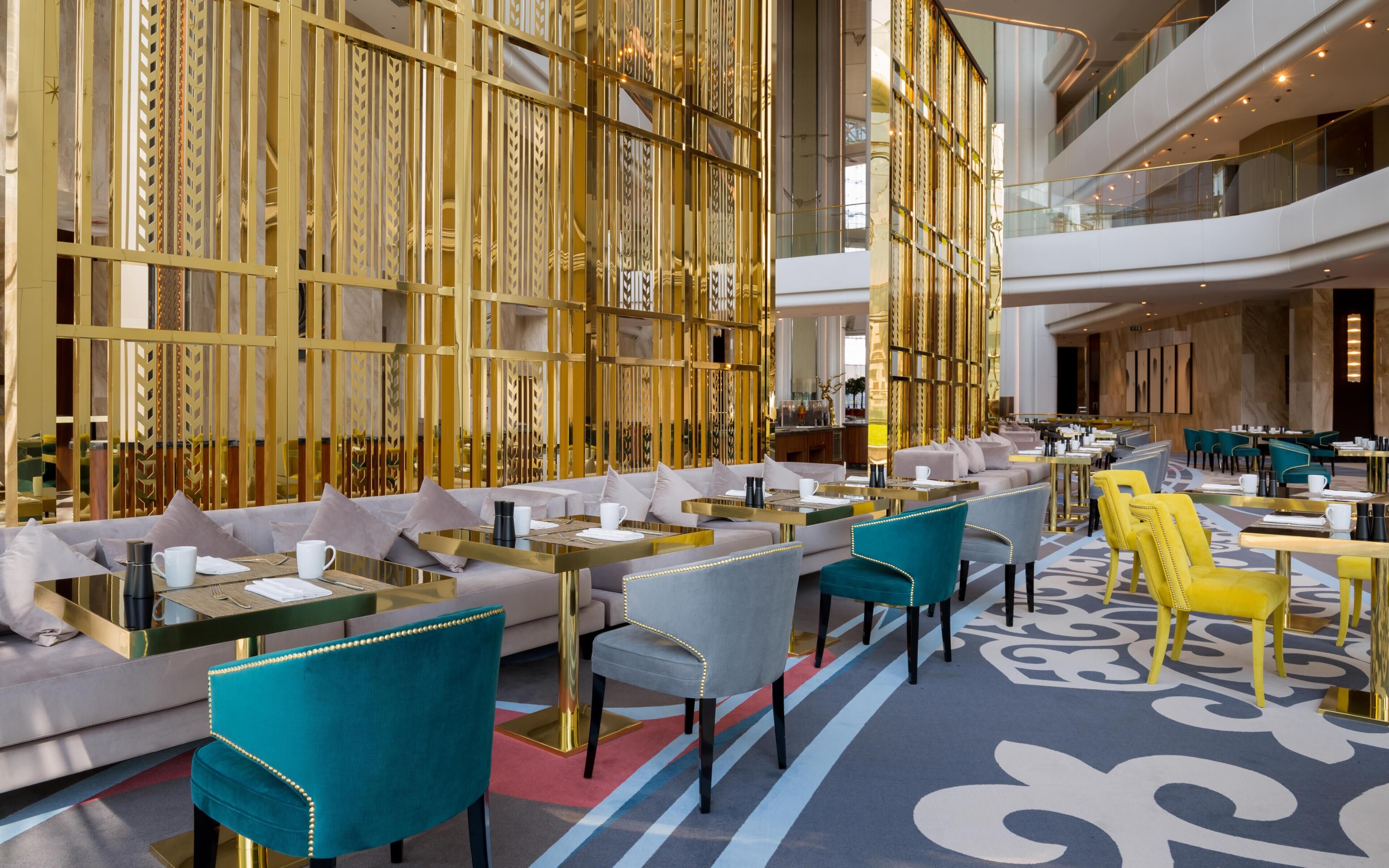 Un moderno vestíbulo de hotel con techo alto, una zona de estar central con sofás y sillones, y una alfombra estampada.