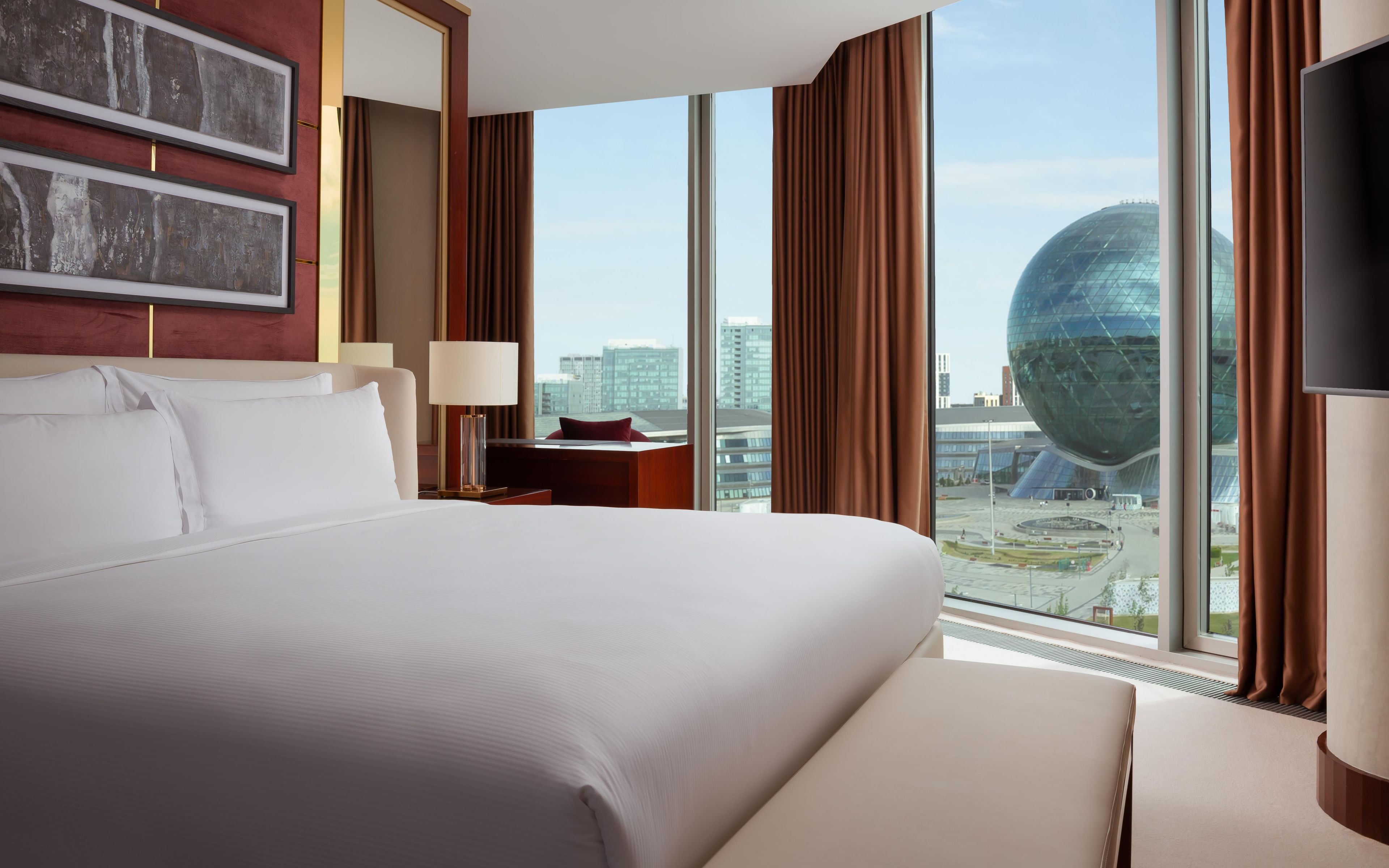 Une chambre d’hôtel avec un grand lit, une table de chevet avec une lampe, une télévision et une vue sur le paysage urbain et un bâtiment remarquable.